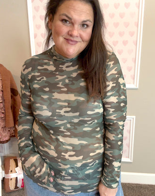 Person wearing a camouflage long-sleeve shirt in a room with a neutral background