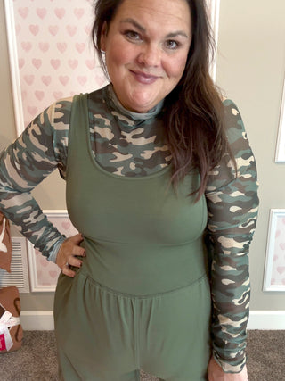 Woman wearing a green dress with camouflage sleeves against a heart-patterned wall.