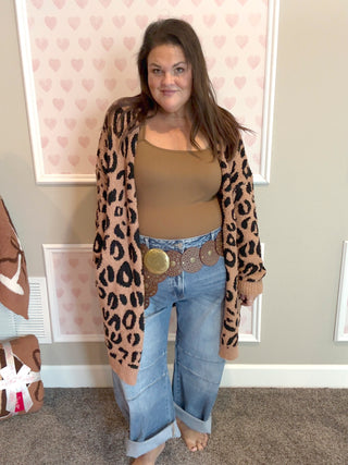 Woman wearing a leopard print cardigan, beige top, and blue jeans indoors.