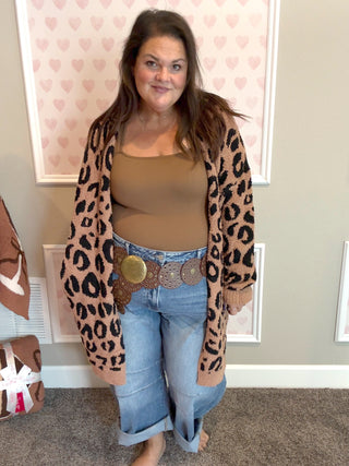 Woman wearing a leopard print cardigan, beige top, and blue jeans indoors.