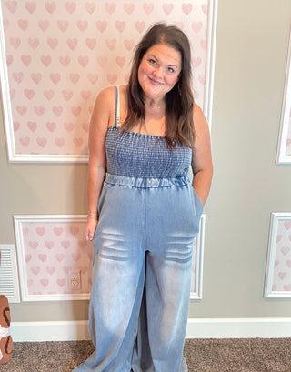 Woman wearing a blue jumpsuit standing in front of a wall with heart patterns.