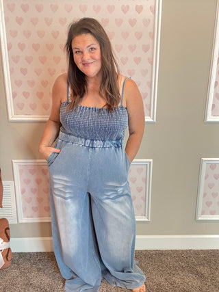 Woman wearing a blue jumpsuit standing in a room with heart-patterned wallpaper.