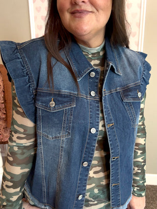 Person wearing a blue denim vest over a camouflage shirt indoors.