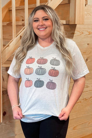 Woman wearing a white t-shirt with colorful pumpkin designs in a wooden staircase setting