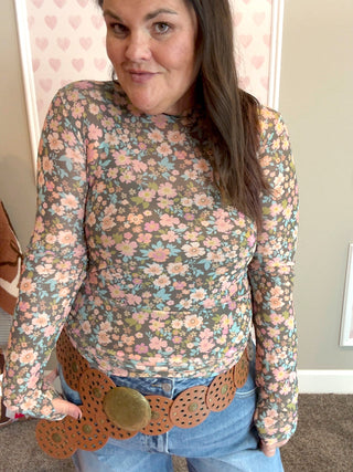 Woman wearing a floral long-sleeve mesh top with a patterned belt.