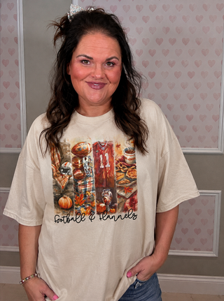A woman wearing a cream-colored graphic t-shirt with a 'Football Channels' print featuring football-themed imagery, posed against a pink heart-patterned wall.