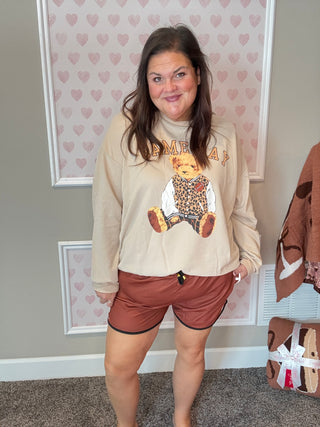 Woman wearing a beige sweatshirt with a graphic design and brown shorts in a room with heart-patterned wallpaper.