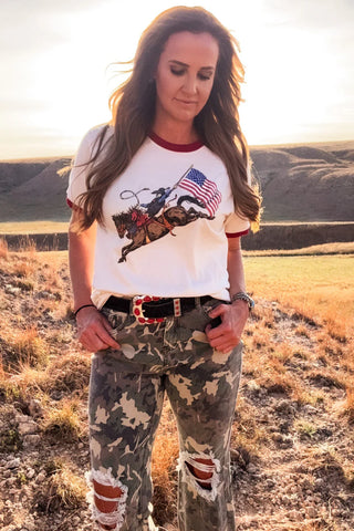 Woman standing in a field wearing a graphic t-shirt and camouflage pants.