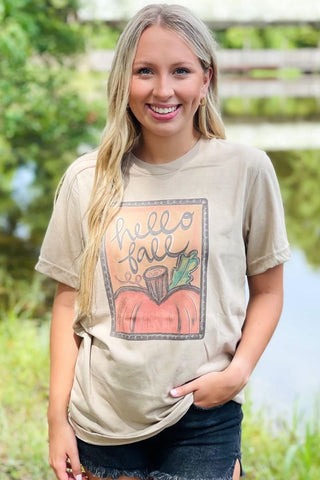 Woman wearing a 'Hello Fall' t-shirt with a pumpkin graphic outdoors.