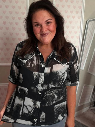 Woman wearing a black and white patterned shirt in a room with heart-shaped wallpaper.