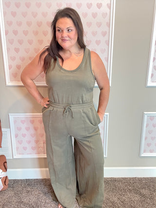 Woman wearing a green jumpsuit in a room with heart-patterned wallpaper.