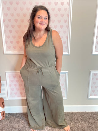 Woman wearing a green jumpsuit standing in a room with heart-patterned wallpaper.