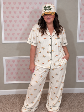 A woman modeling a two-piece pajama set with a white base and a colorful fish pattern, paired with a matching baseball cap that reads 'Happy Camper'.