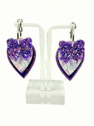 Heart-shaped purple glitter earrings on a white stand