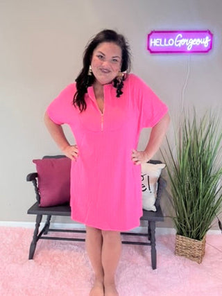 Woman wearing a pink dress standing in a room with a plant and bench.