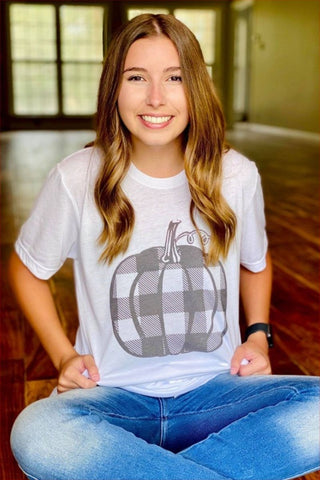 Person wearing a white t-shirt with a pumpkin graphic, sitting indoors.