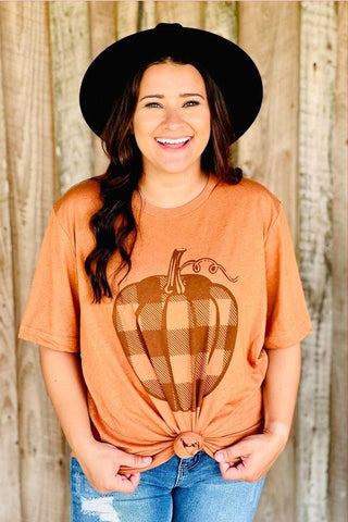Woman wearing an orange t-shirt with a pumpkin design, black hat, and blue jeans against a wooden background.