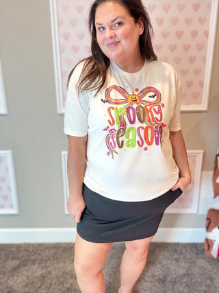Person wearing a white t-shirt with colorful text and graphics, standing in a room with heart-patterned wallpaper.