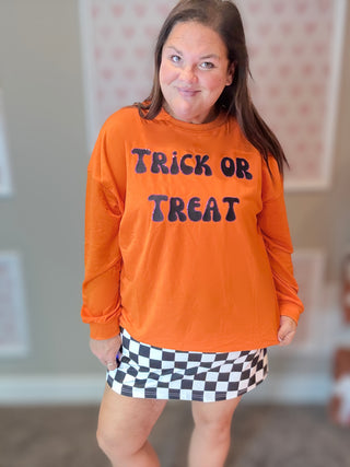 Person wearing an orange 'Trick or Treat' shirt with a checkered skirt indoors.