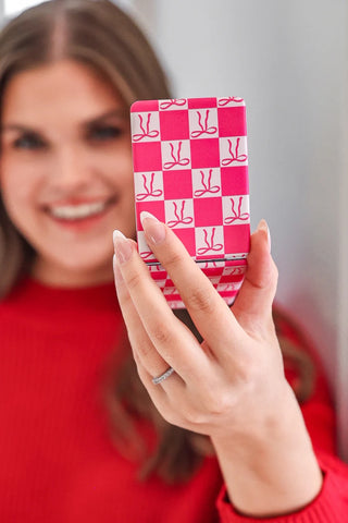 Person holding a pink and white checkered phone case with a pattern of bows.