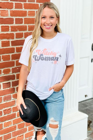 Woman wearing a 'Woman' t-shirt holding a black cowboy hat against a brick wall.