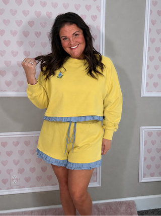 Yellow ruffle lounge set with cropped sweatshirt and matching shorts in a soft pastel yellow with blue trim details.